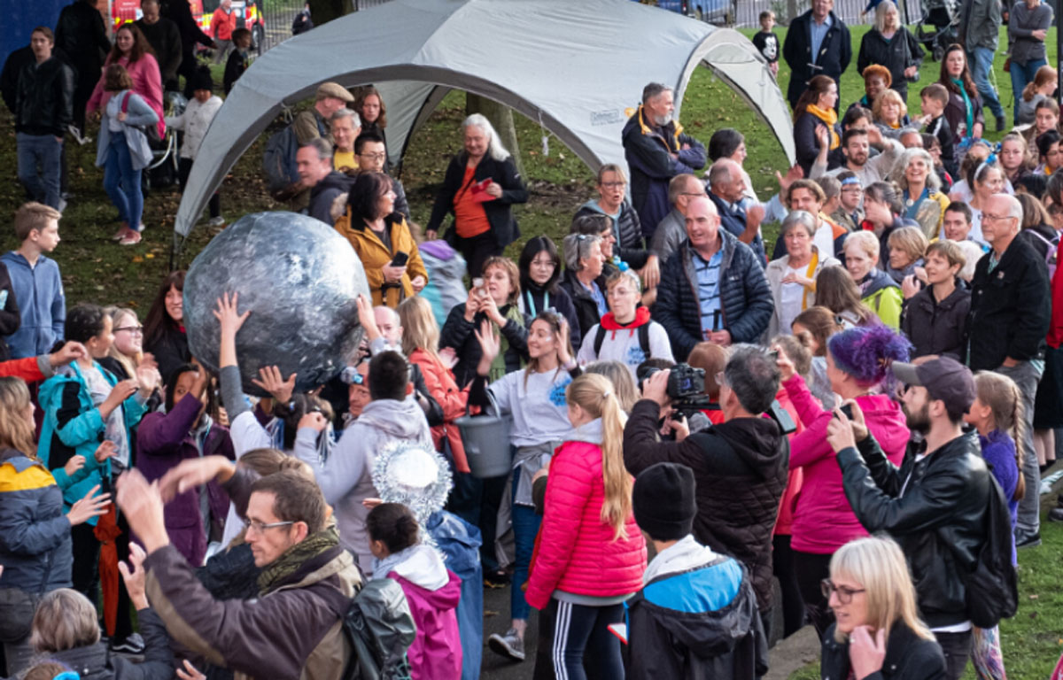 Large group of families stood on grass next to small tent, one is holding a sculpture of the moon