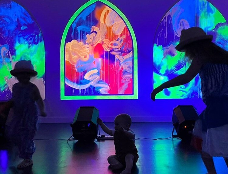 A baby and children in 'Goo Gaa Gallery' with artworks animated by UV light.