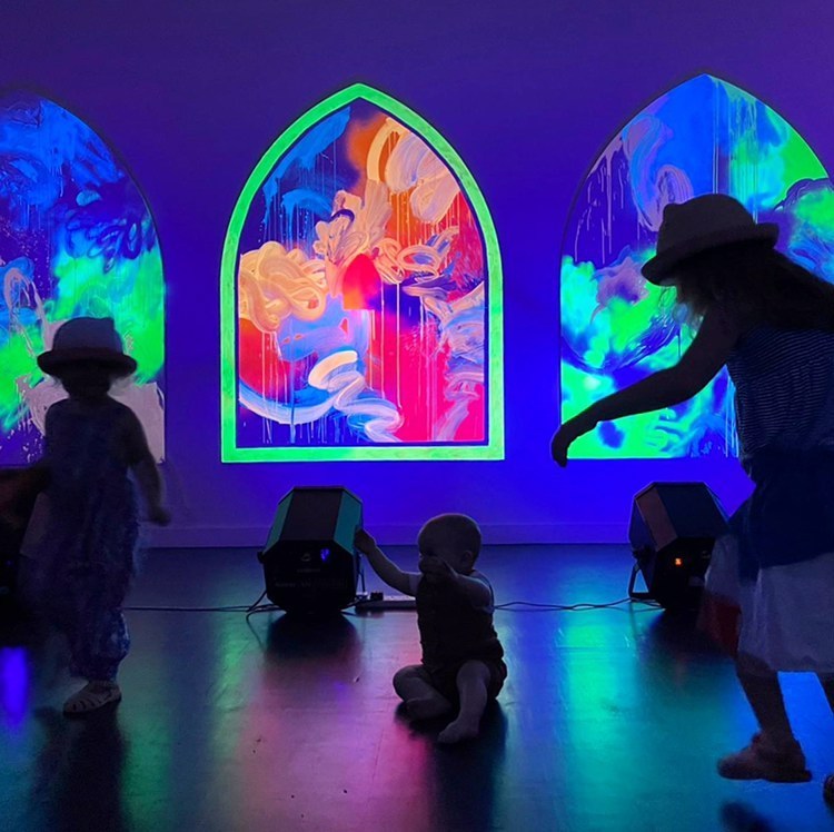 A baby and children in 'Goo Gaa Gallery' with artworks animated by UV light.