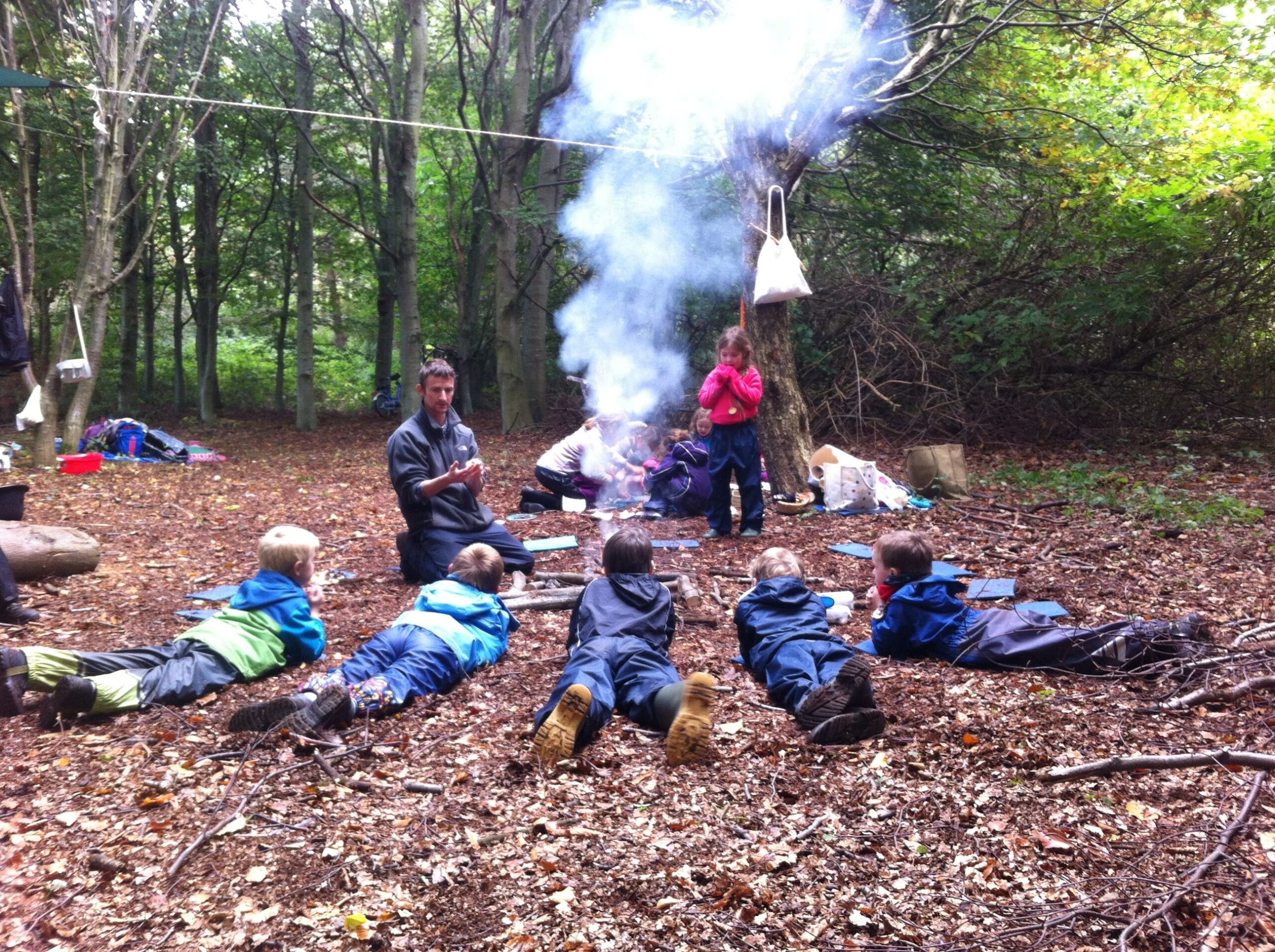 An adult is telling children stories by the campire in the woods.