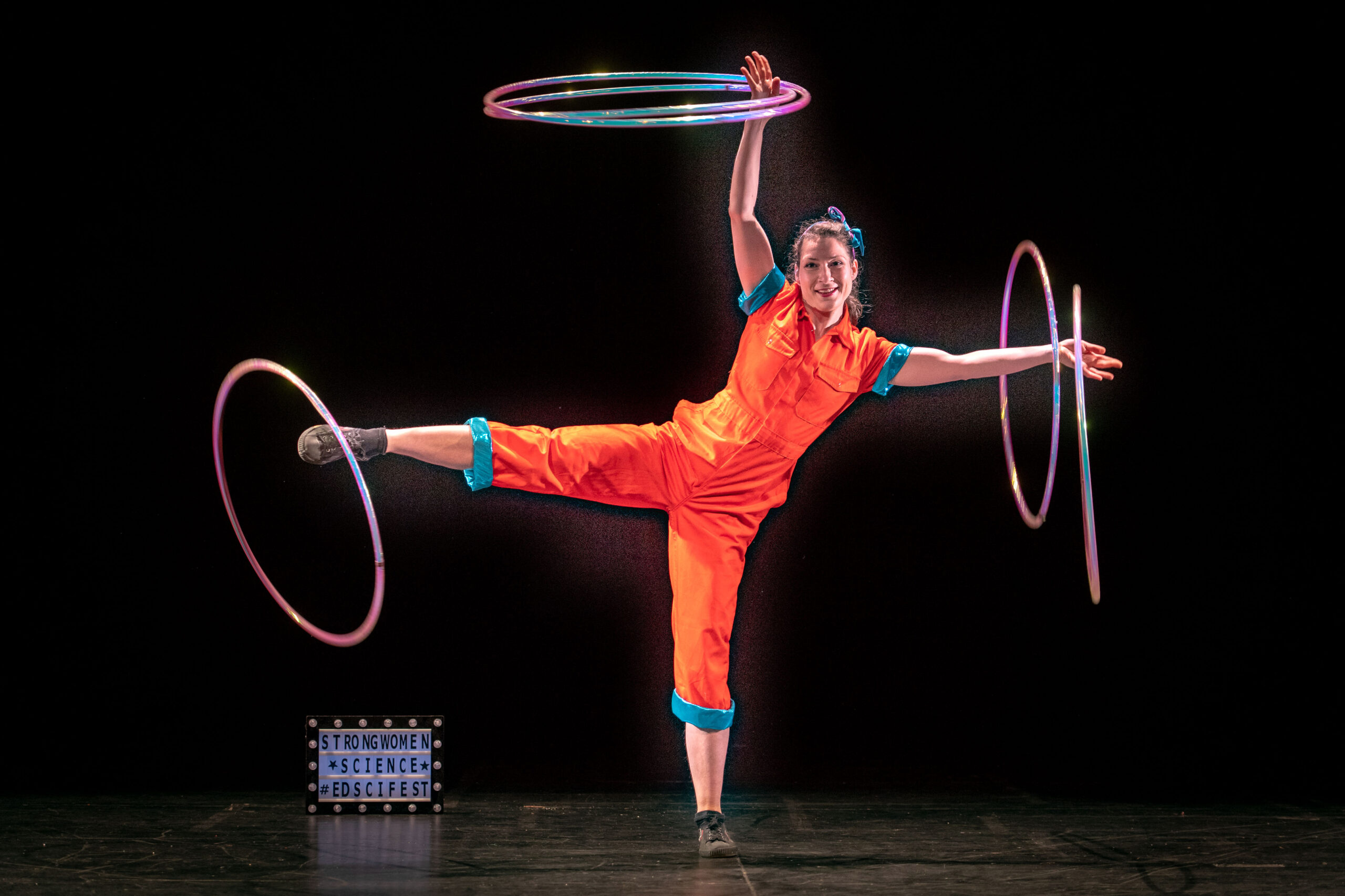 A circus performer balancing rings on her arms and right leg, on stage at the Strong Women Science show.