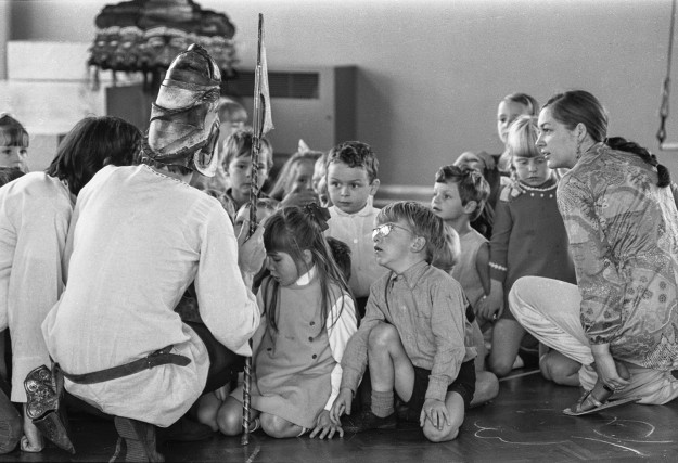 Black and white photograph of costumed performers interacting with children, representing early days of theatre for children.