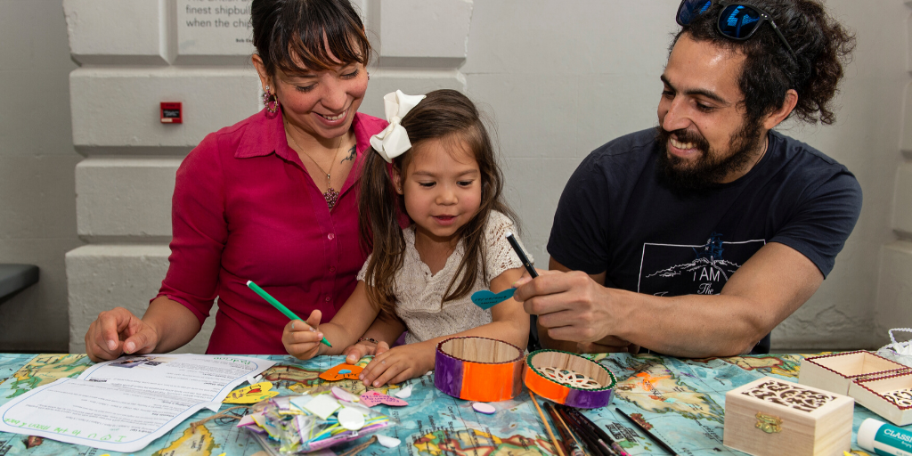 Two parents or guardians get creative at a craft table with a little girl