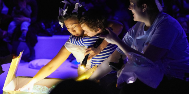 A person holding a child is reaching into a box with light emanating from it