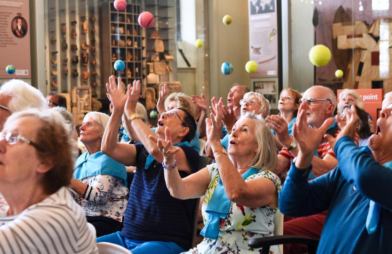 Audience of older visitors preparing to catch different coloured tennis balls